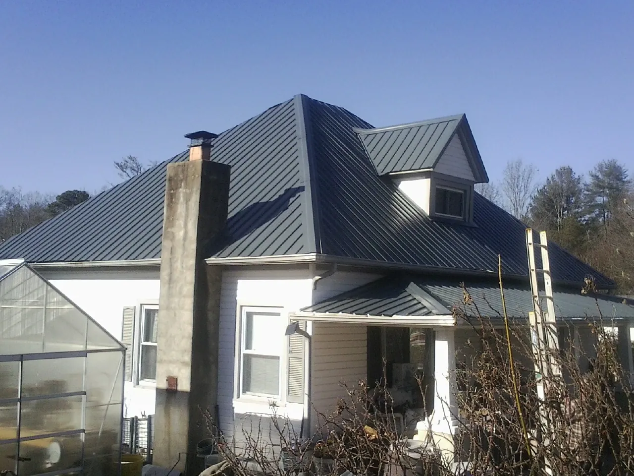 Dark blue standing seam metal roof on a white farmhouse with dormer — Slate & Tile Roof Repair by Roofing Brothers in Meeker