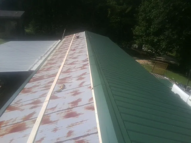 Old rusted panels beside newly installed green metal roofing — Wind Damage Roof Repair by Roofing Brothers in Meeker