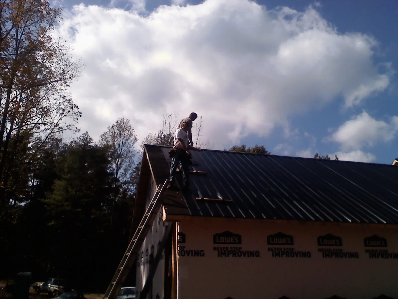Roofer fastening dark metal panels high against a cloudy sky, from a Roof Inspection job in Meeker